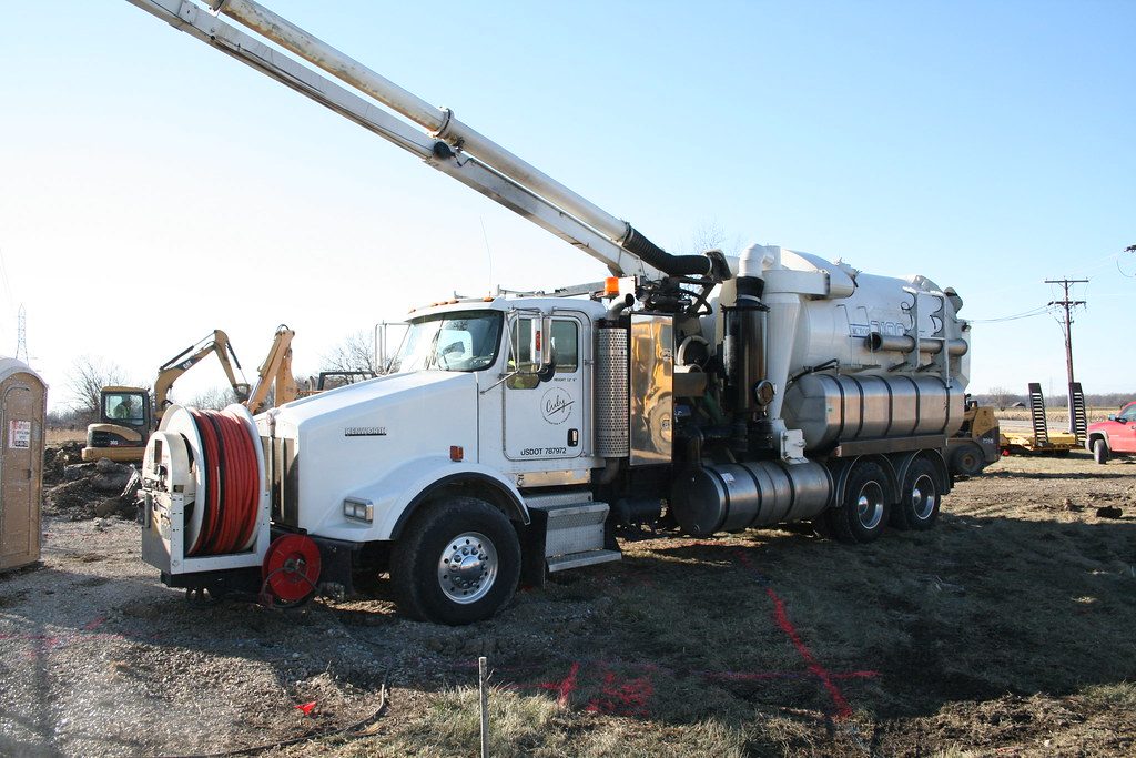 Hydrovac truck with its boom raised on a dirt job site, fresh locate paint on the ground in front of it