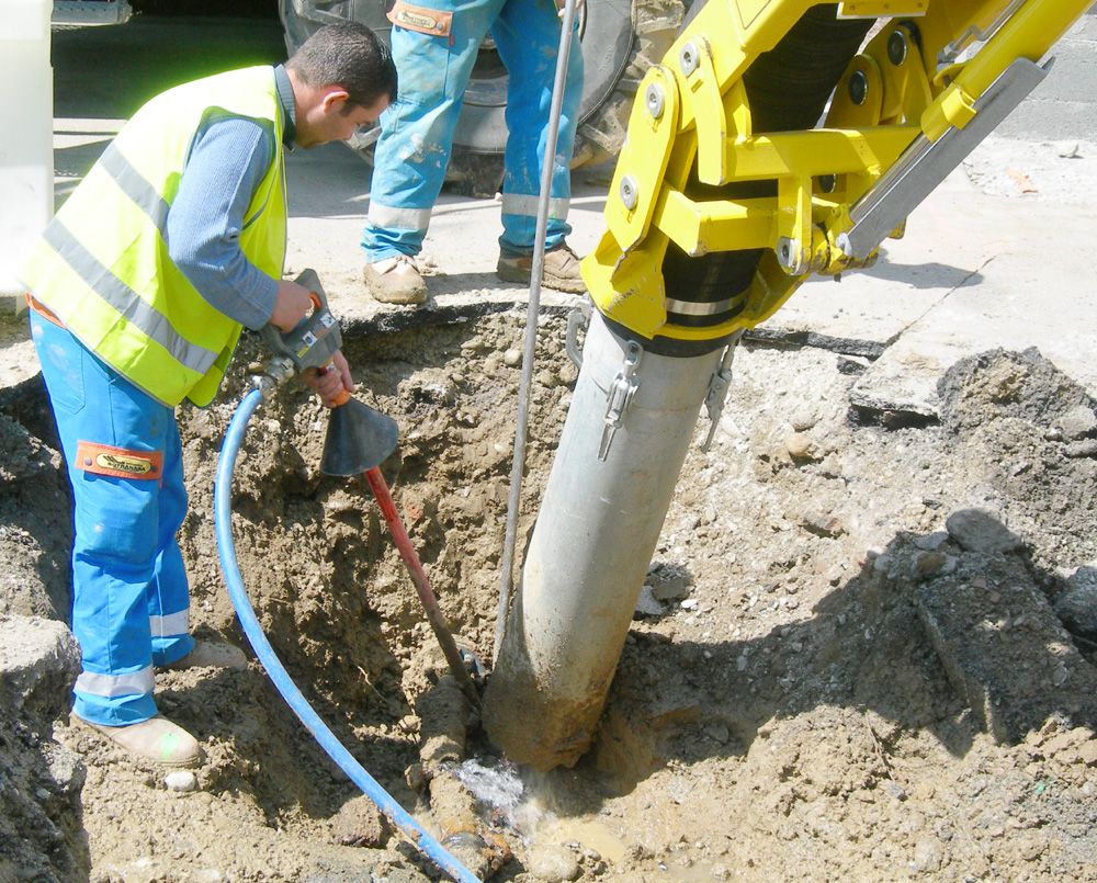 Worker guiding a vacuum excavation hose into a narrow trench where buried service lines are exposed